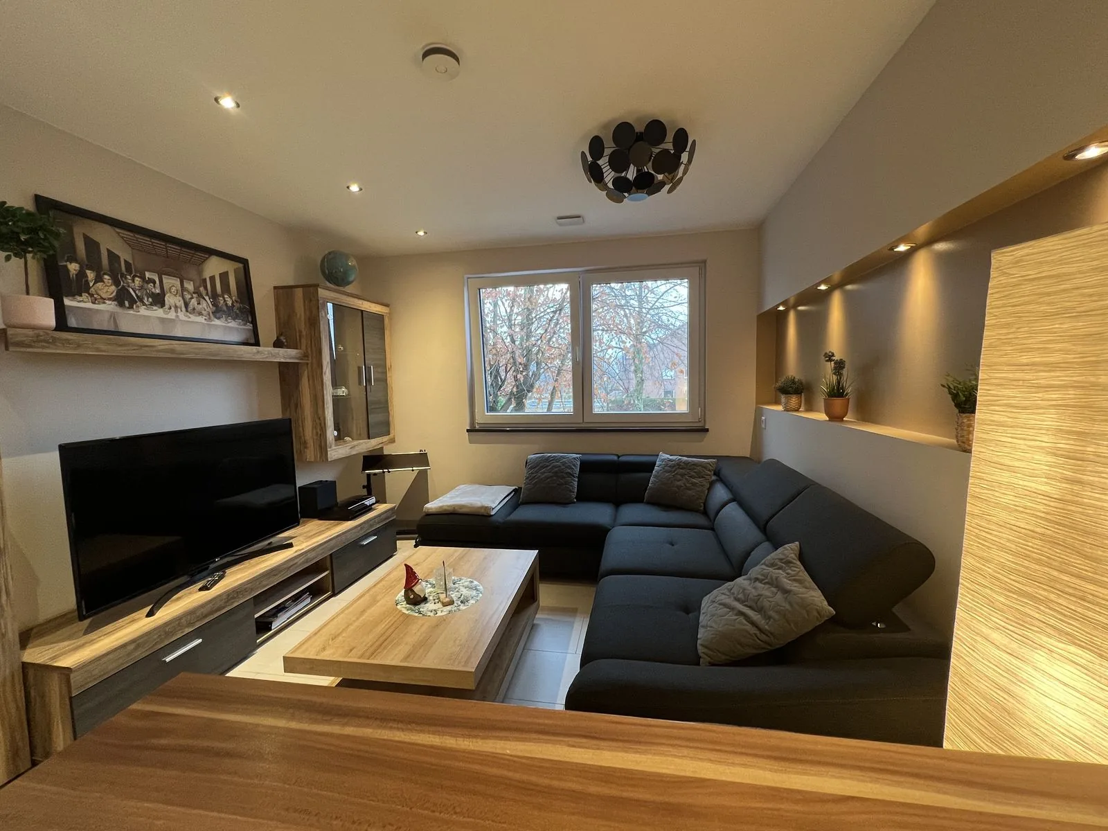Wohnzimmer mit großer Couch, Fernseher und warmem Licht im Deluxe Apartment Eins