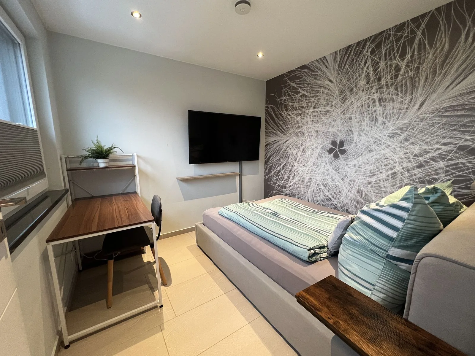 Schlafzimmer mit Fernseher, Schreibtisch und moderner Fototapete im Deluxe Apartment Eins