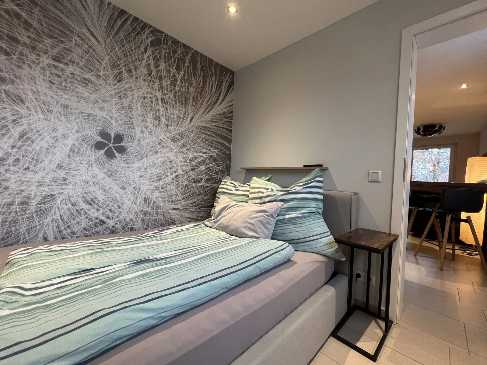 Bett mit frischer Wäsche und Blick in den Wohnbereich im Deluxe Apartment Eins