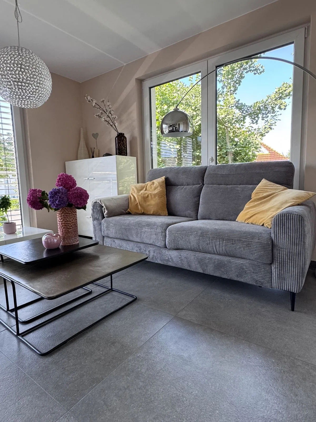 Wohnzimmer mit Sofa, Stehlampe und großen Fenstern im Deluxe Apartment Zwei
